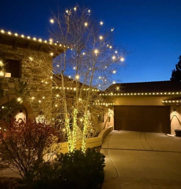 Stone home and garage with warm white roofline and lit aspens at blue hour
