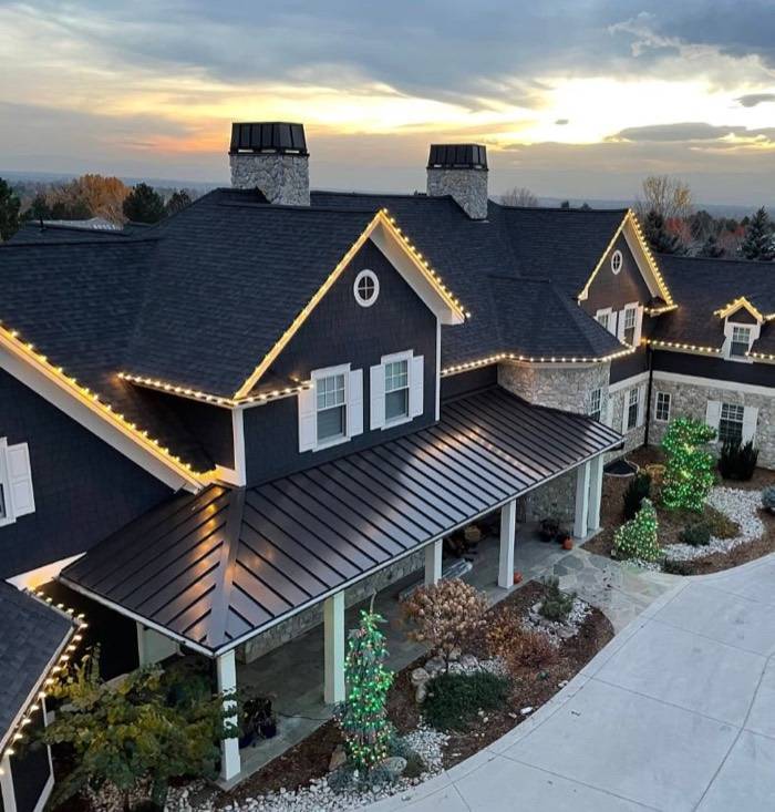 Large home at dusk with warm white roofline and a lit garden tree